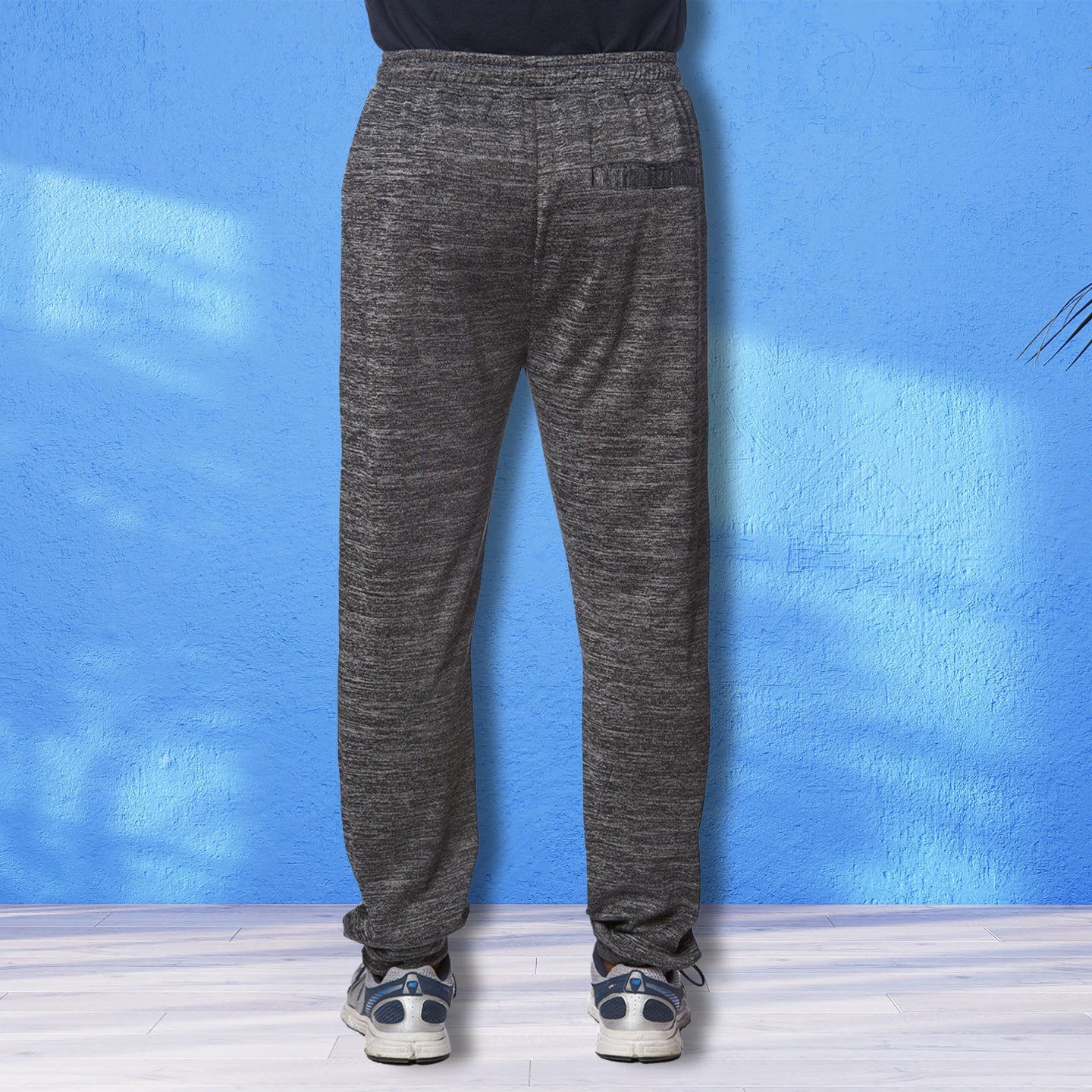 Back view of Carbon Drift Performance Joggers by YOLO Sport Activewear in dark gray, modeled with sneakers against a blue background.