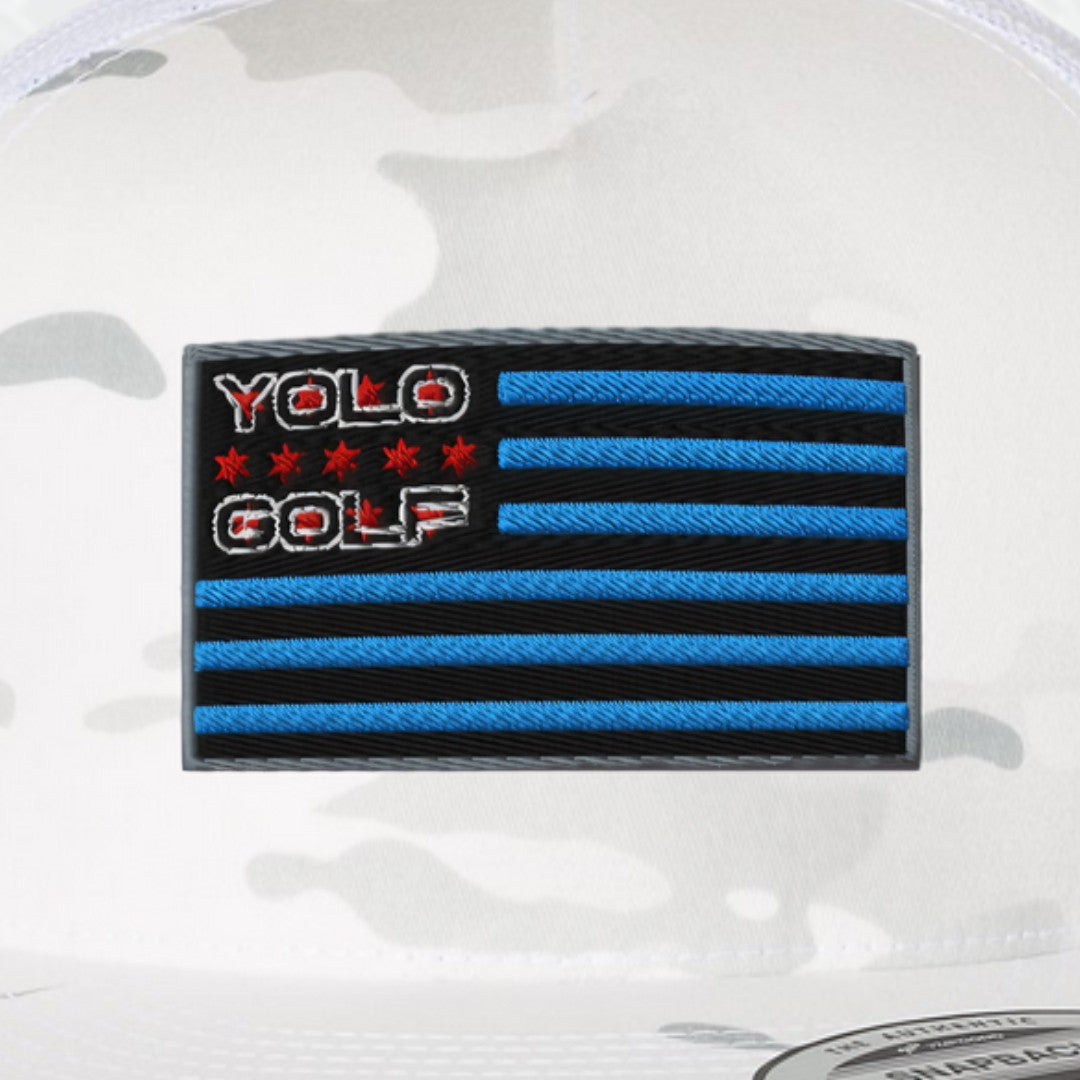 Close-up of #YOLO Golf-USA Flag Multi-Camo Alpine White Trucker Hat showcasing the detailed embroidered blue and black USA flag design on the front panel.