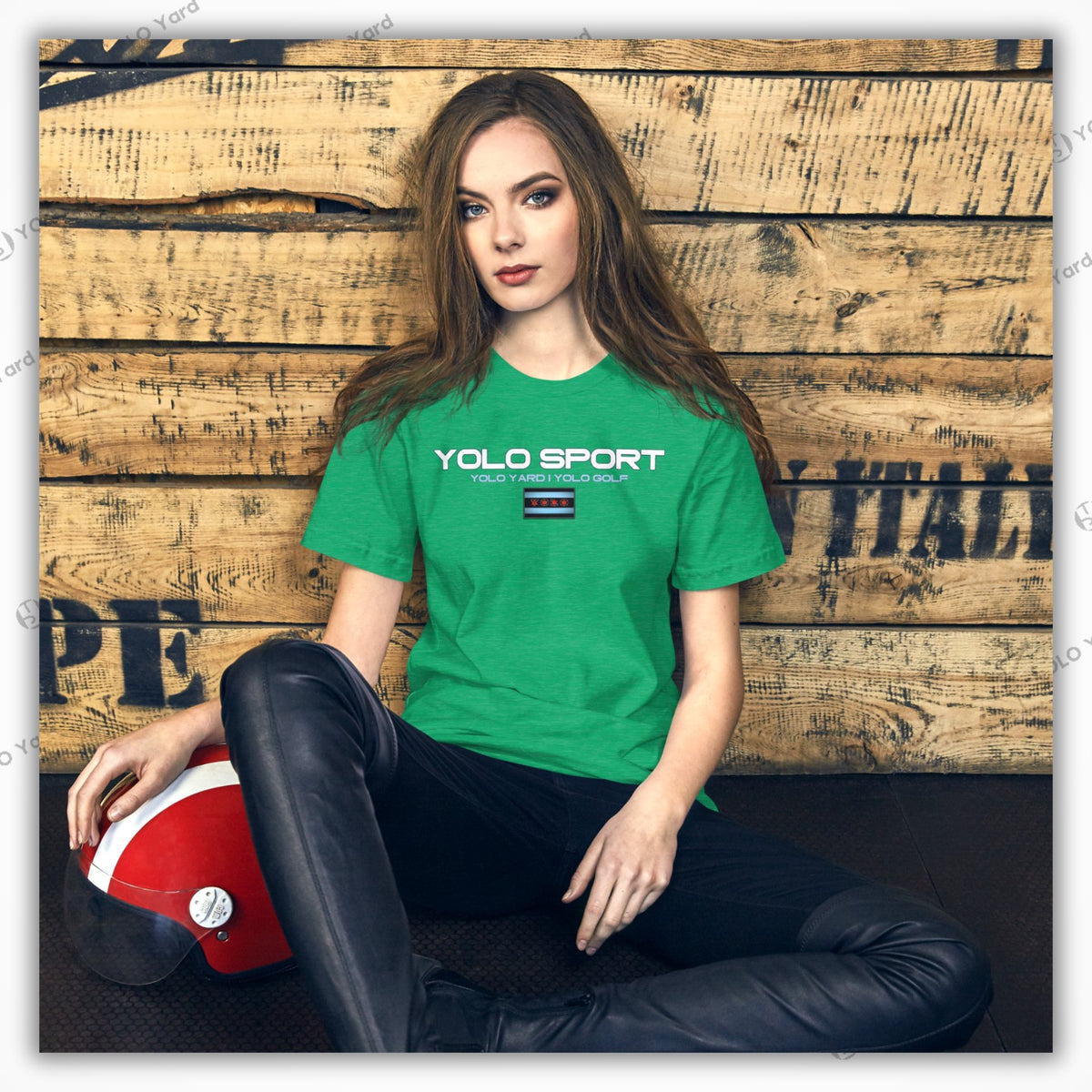 Green YOLO Sport unisex t-shirt worn by a woman seated against a rustic wooden backdrop. Comfortable and stylish for casual wear.