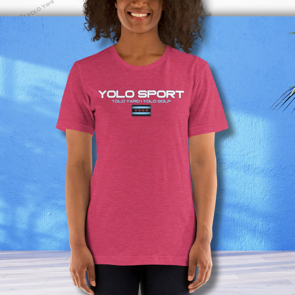 Pink YOLO Sport unisex t-shirt worn by a woman against a blue wall. Lightweight and breathable fabric for casual or active use.