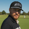 Man wearing a black 'Out of Office' golf rope cap with silver #YOLO Golf embroidery, styled for a trendy golf course look.