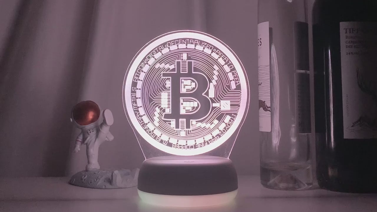 Soft white-lit Bitcoin 3D LED desk lamp on a table with decorative items, creating a cozy and modern ambiance.