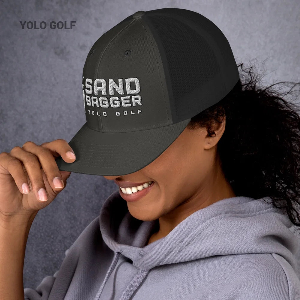 Dark gray Sandbagger trucker hat worn by a smiling woman, highlighting its 