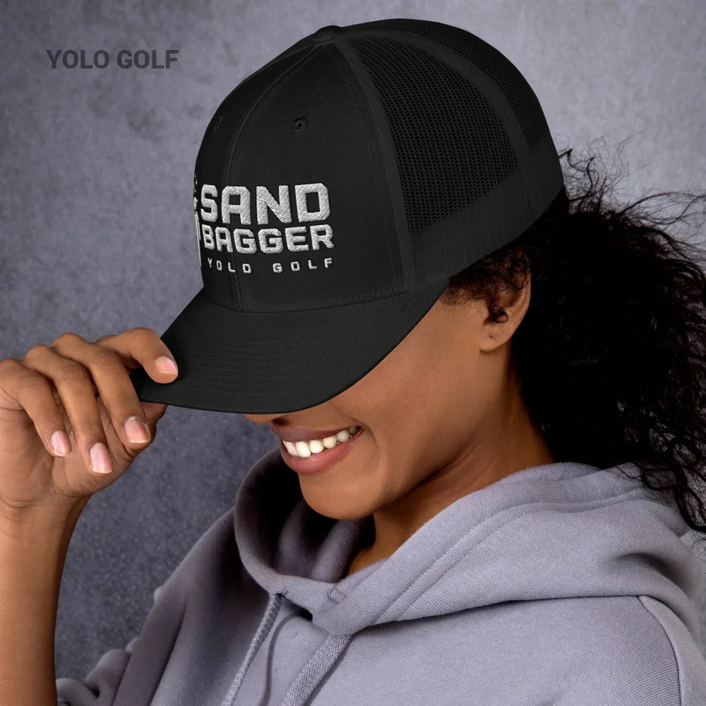 Black Sandbagger trucker hat worn by a smiling woman, featuring an 